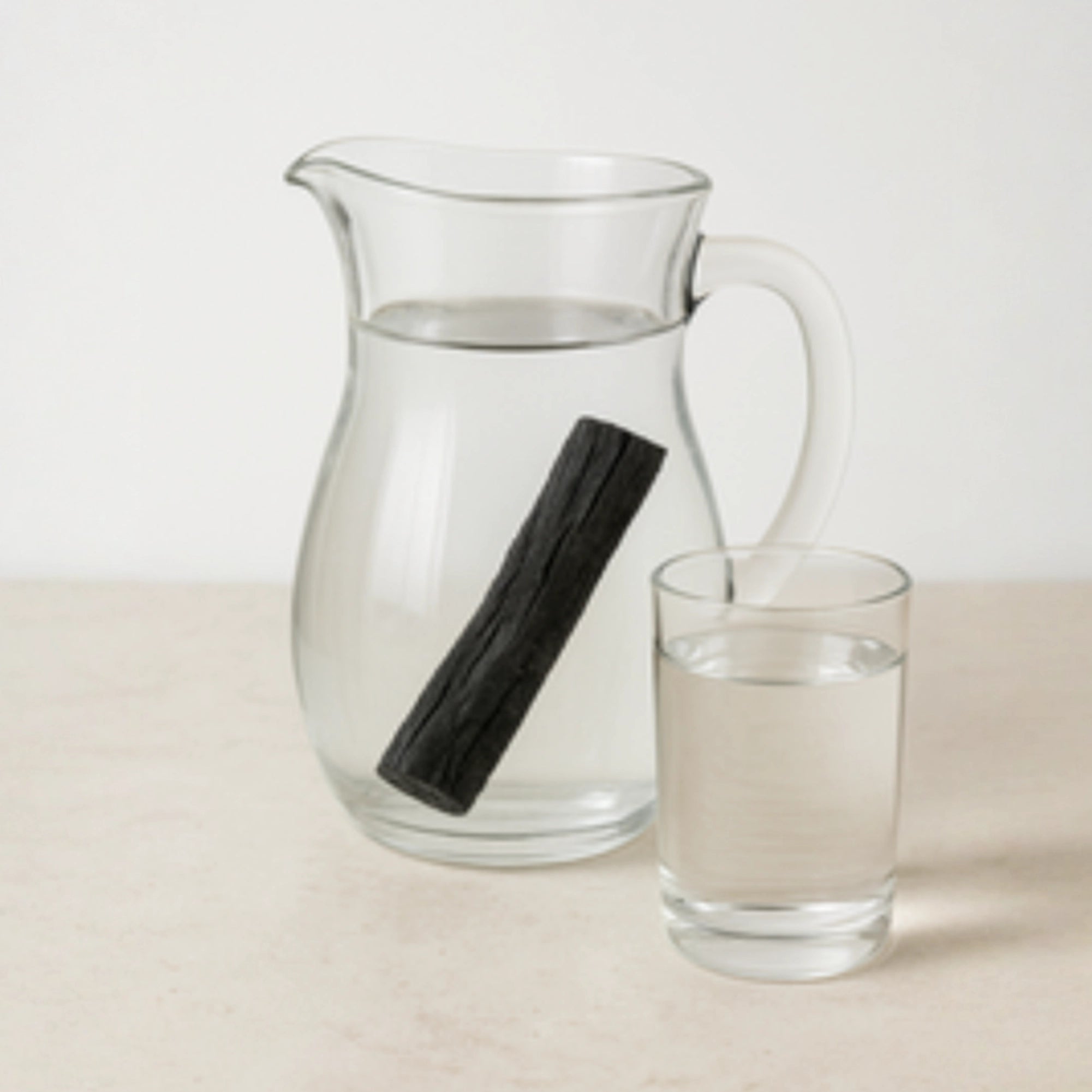 Carafe d'eau contenant un charbon binchotan pour purifier l'eau ainsi qu'un verre d'eau rempli 